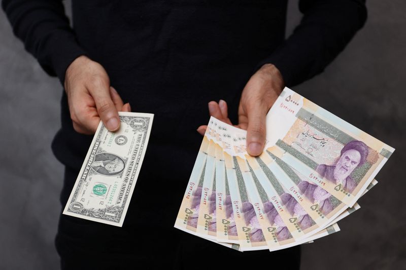 © Reuters. FILE PHOTO: A currency dealer poses for a photo with a U.S one dollar bill and the amount being given when converting it into Iranian rials in an exchange shop in Tehran, Iran December 25, 2022. Majid Asgaripour/WANA (West Asia News Agency) via REUTERS/File Photo